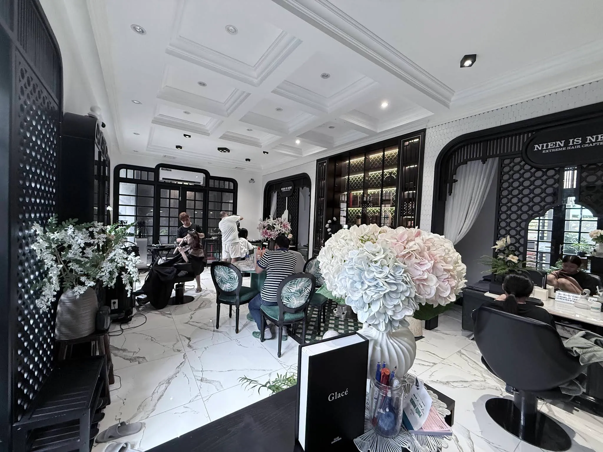 Bright salon floor with white marble, black Indochine lattice arches and palm-print chairs at Nien Is New in Da Nang